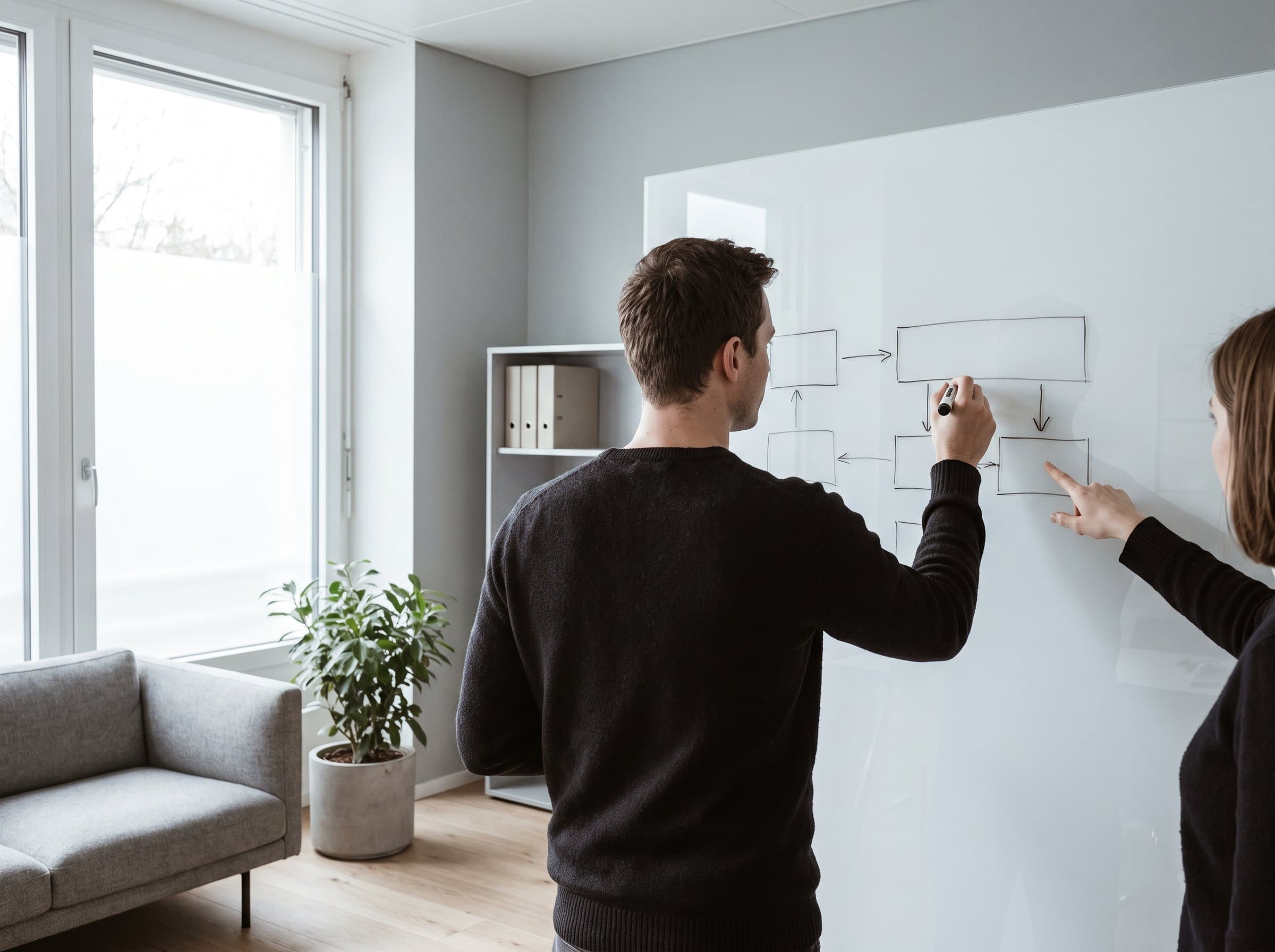 Zwei Personen am Whiteboard, eine zeichnet Kästchen und Pfeile